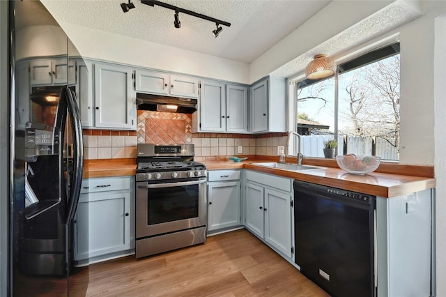 kitchen with wooden counters, light wood-style floors, a sink, under cabinet range hood, and black appliances