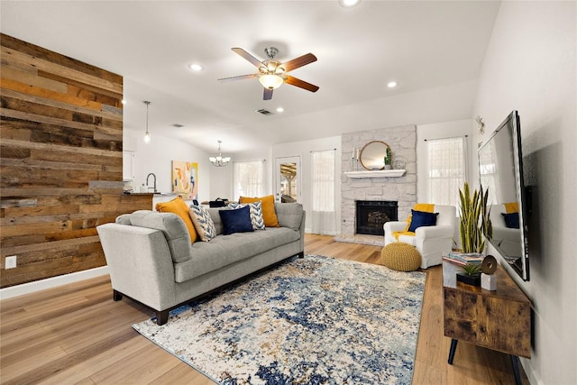 living area featuring lofted ceiling, a stone fireplace, and light wood-style flooring