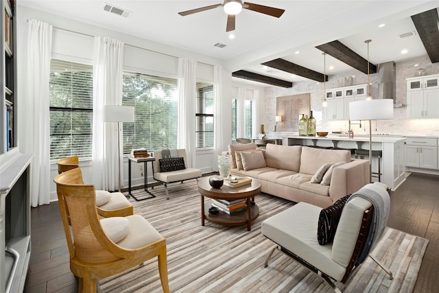 living area with a healthy amount of sunlight, visible vents, beamed ceiling, and hardwood / wood-style flooring