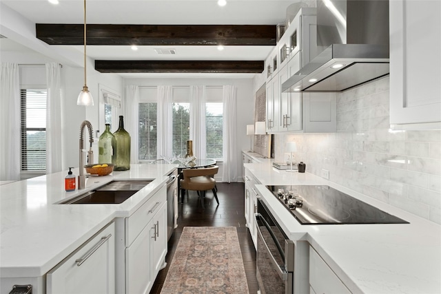 kitchen featuring backsplash, appliances with stainless steel finishes, white cabinetry, a sink, and wall chimney range hood