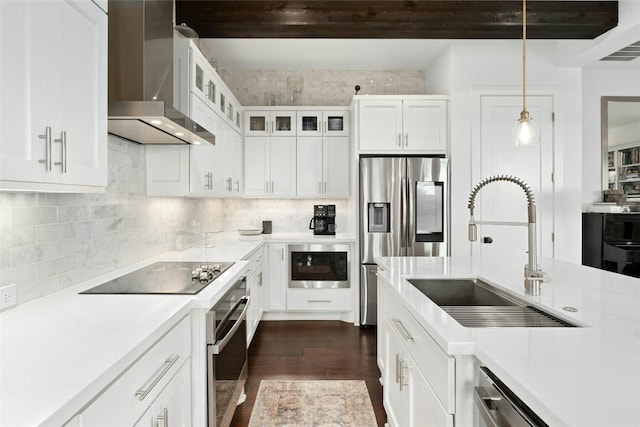 kitchen with a sink, stainless steel appliances, wall chimney range hood, white cabinetry, and backsplash