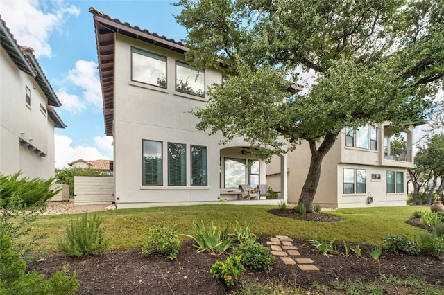 rear view of property featuring a ceiling fan, a lawn, a patio, and stucco siding