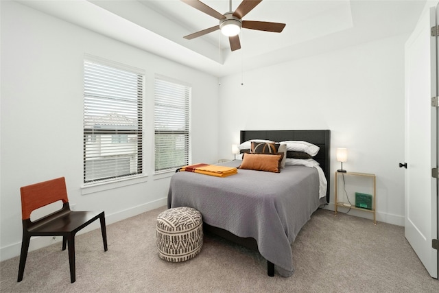 bedroom featuring light carpet, a tray ceiling, and baseboards