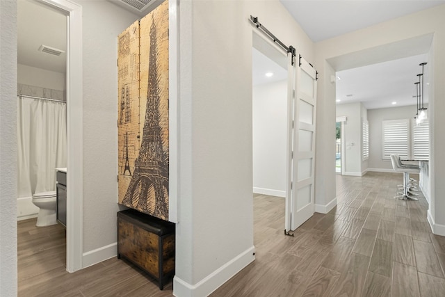 corridor featuring visible vents, wood finished floors, a barn door, baseboards, and recessed lighting
