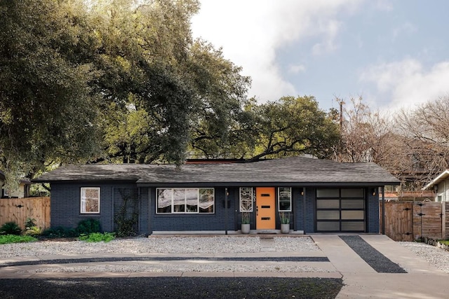 view of front facade featuring a garage, brick siding, fence, and driveway