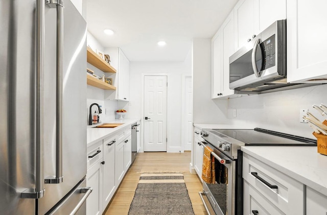 kitchen with open shelves, appliances with stainless steel finishes, a sink, and white cabinetry