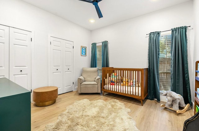 bedroom featuring a crib, a ceiling fan, wood finished floors, and recessed lighting