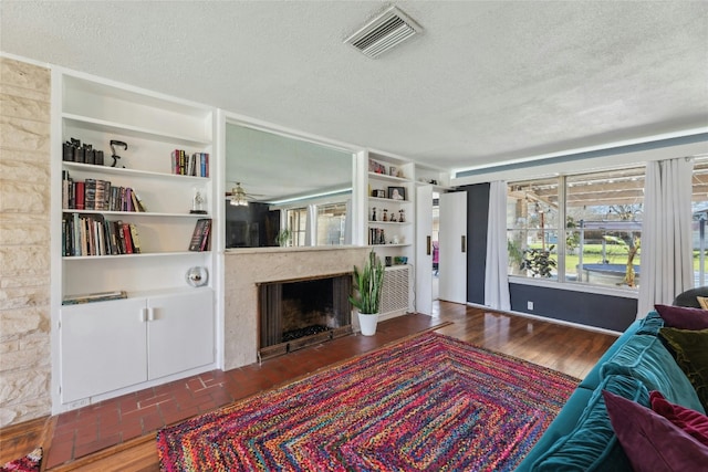 living room featuring built in features, visible vents, wood finished floors, a textured ceiling, and a fireplace