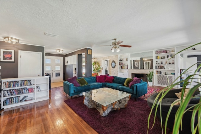 living area featuring a fireplace, visible vents, a ceiling fan, a textured ceiling, and hardwood / wood-style floors