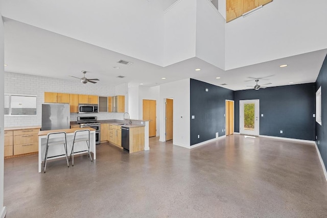 kitchen with visible vents, a towering ceiling, appliances with stainless steel finishes, light brown cabinets, and a sink