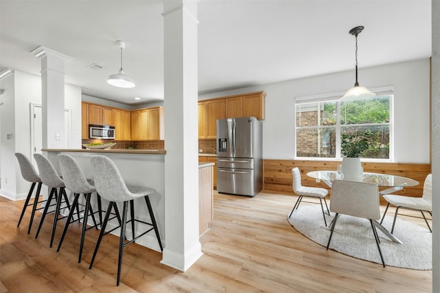 kitchen with a breakfast bar area, appliances with stainless steel finishes, light wood-type flooring, ornate columns, and backsplash