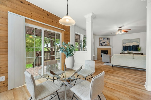 dining area featuring ceiling fan, a fireplace, wood finished floors, and ornate columns