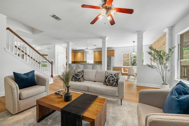 living room featuring decorative columns, visible vents, light wood-style flooring, a ceiling fan, and stairs