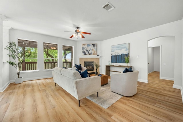 living area with arched walkways, visible vents, baseboards, light wood-style floors, and a glass covered fireplace