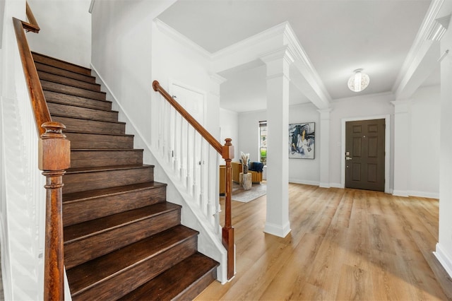 entryway featuring crown molding, ornate columns, stairway, light wood-style floors, and baseboards