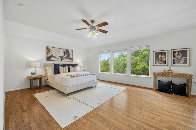 bedroom featuring ceiling fan, baseboards, a raised ceiling, and wood finished floors