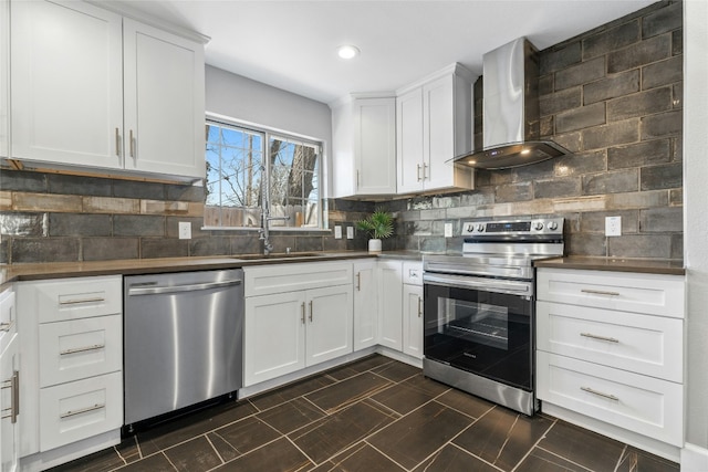 kitchen featuring tasteful backsplash, appliances with stainless steel finishes, white cabinets, a sink, and wall chimney exhaust hood