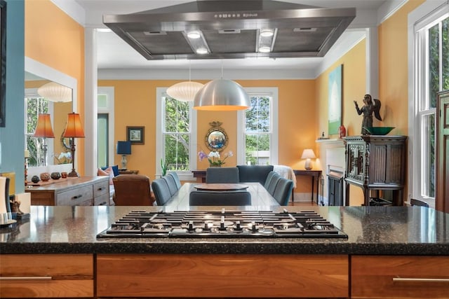 kitchen with exhaust hood, dark stone counters, brown cabinets, stainless steel gas cooktop, and open floor plan