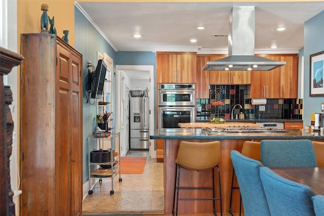 kitchen with island exhaust hood, a kitchen breakfast bar, brown cabinets, tasteful backsplash, and appliances with stainless steel finishes
