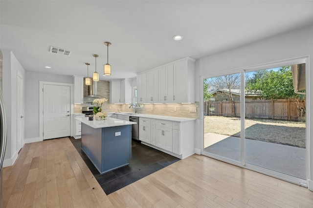 kitchen with visible vents, white cabinets, wall chimney range hood, appliances with stainless steel finishes, and backsplash