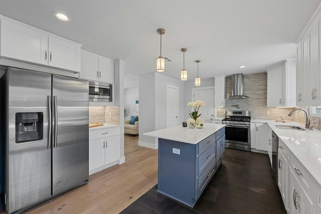 kitchen with wall chimney exhaust hood, appliances with stainless steel finishes, a sink, and white cabinets