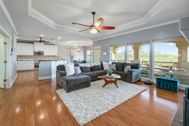 living area featuring a ceiling fan, a tray ceiling, wood finished floors, and ornamental molding