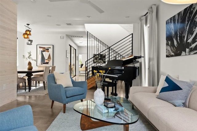 living area featuring visible vents, finished concrete floors, a ceiling fan, wood walls, and stairs