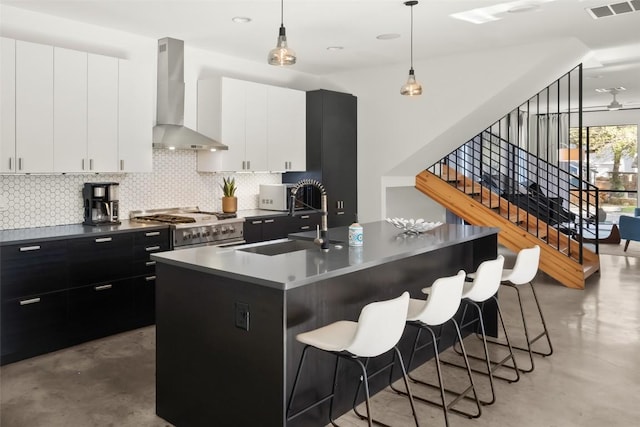 kitchen with finished concrete flooring, a sink, gas range, dark cabinets, and wall chimney exhaust hood