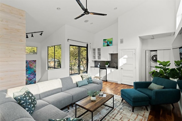 living area featuring light wood finished floors, a ceiling fan, stacked washer and clothes dryer, rail lighting, and high vaulted ceiling