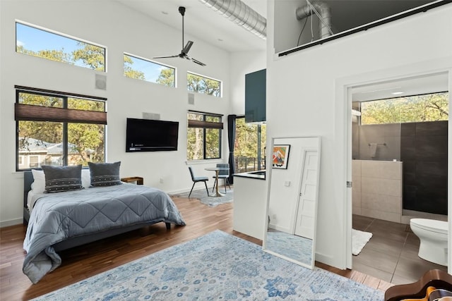 bedroom featuring multiple windows, a towering ceiling, baseboards, and wood finished floors