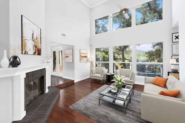 living room with a fireplace, a ceiling fan, visible vents, baseboards, and dark wood finished floors