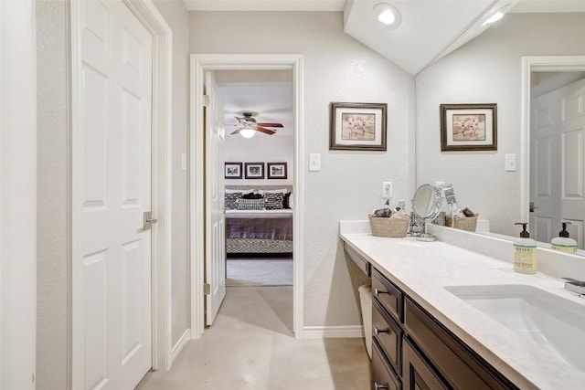 ensuite bathroom featuring lofted ceiling, ceiling fan, vanity, baseboards, and ensuite bath