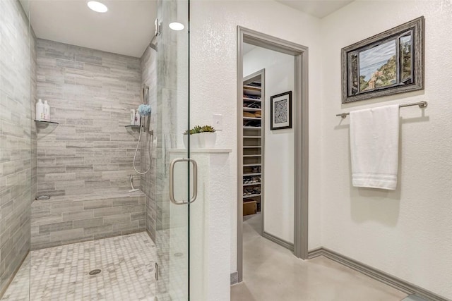 bathroom with a spacious closet, a shower stall, and finished concrete floors