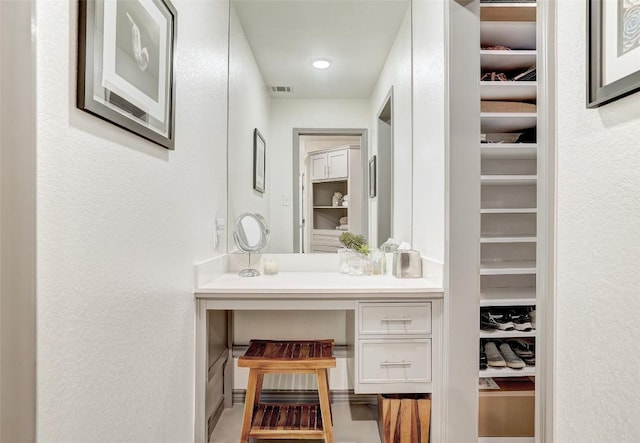 bathroom with a textured wall, vanity, visible vents, and a walk in closet