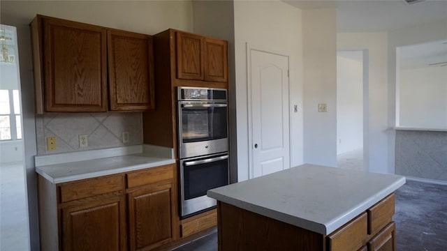 kitchen with a center island, tasteful backsplash, light countertops, brown cabinetry, and stainless steel double oven