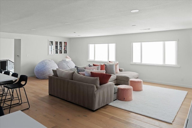 living area featuring visible vents, light wood-style flooring, baseboards, and a textured ceiling