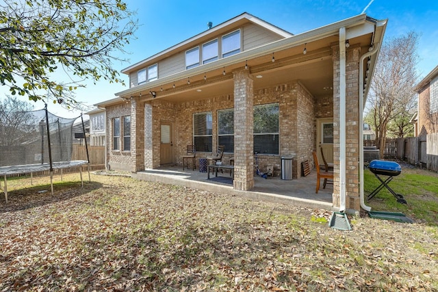 rear view of property with a trampoline, brick siding, a fenced backyard, a patio area, and entry steps