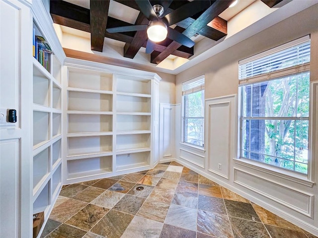 unfurnished room featuring stone tile floors, ceiling fan, a decorative wall, coffered ceiling, and beamed ceiling