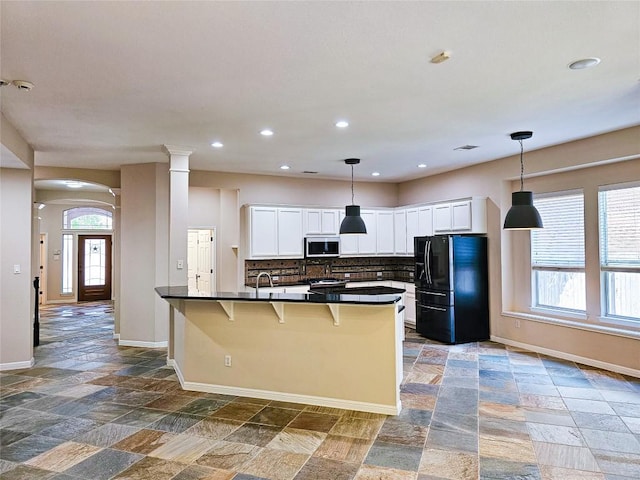 kitchen with black fridge with ice dispenser, stainless steel microwave, dark countertops, baseboards, and stone tile floors