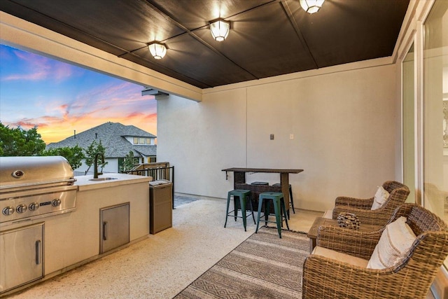 patio terrace at dusk with a balcony, a grill, an outdoor kitchen, and a sink