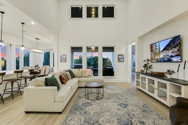 living area featuring an inviting chandelier, light wood-style flooring, and a high ceiling