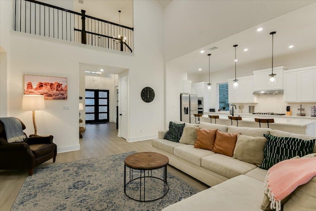 living area with light wood-style floors, recessed lighting, baseboards, and a high ceiling