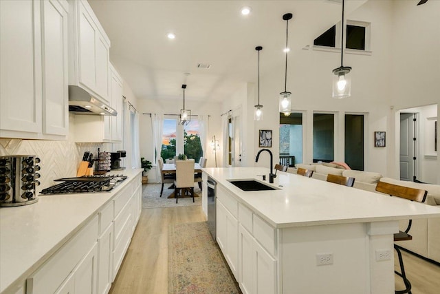 kitchen with under cabinet range hood, a breakfast bar, a sink, appliances with stainless steel finishes, and tasteful backsplash