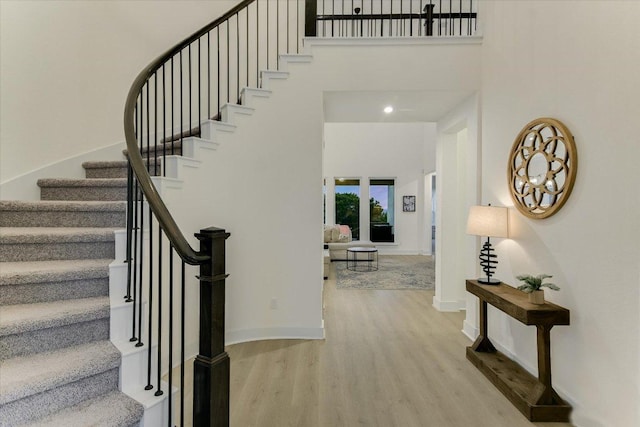 interior space featuring light wood-type flooring, a towering ceiling, and baseboards