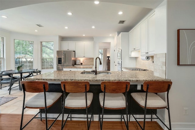 kitchen featuring visible vents, appliances with stainless steel finishes, a peninsula, white cabinetry, and a sink