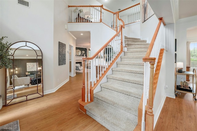 staircase featuring visible vents, a towering ceiling, baseboards, and wood finished floors