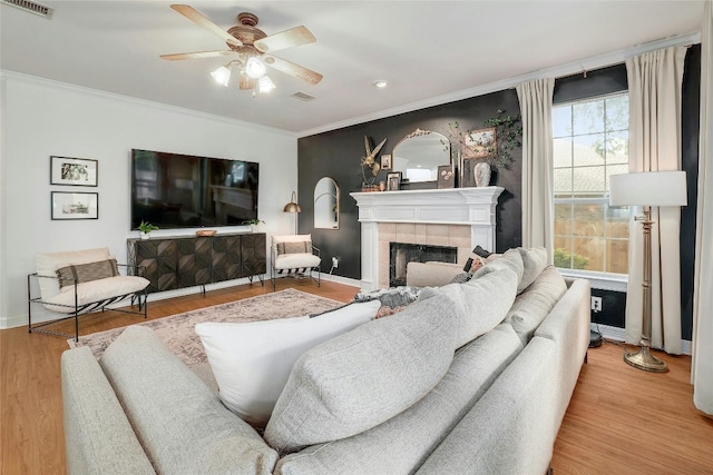 living area with crown molding, a fireplace, visible vents, wood finished floors, and baseboards