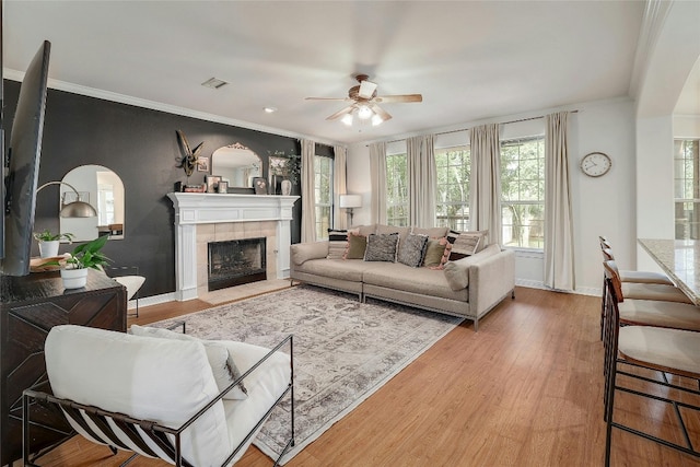 living room featuring baseboards, visible vents, a tiled fireplace, wood finished floors, and crown molding