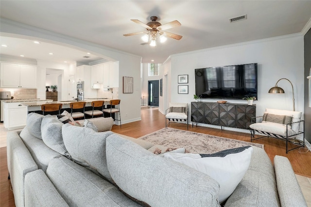 living area with visible vents, baseboards, ceiling fan, ornamental molding, and light wood-type flooring