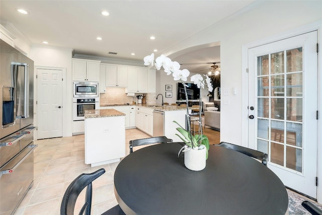 kitchen featuring white cabinets, decorative backsplash, a center island, stainless steel appliances, and a sink